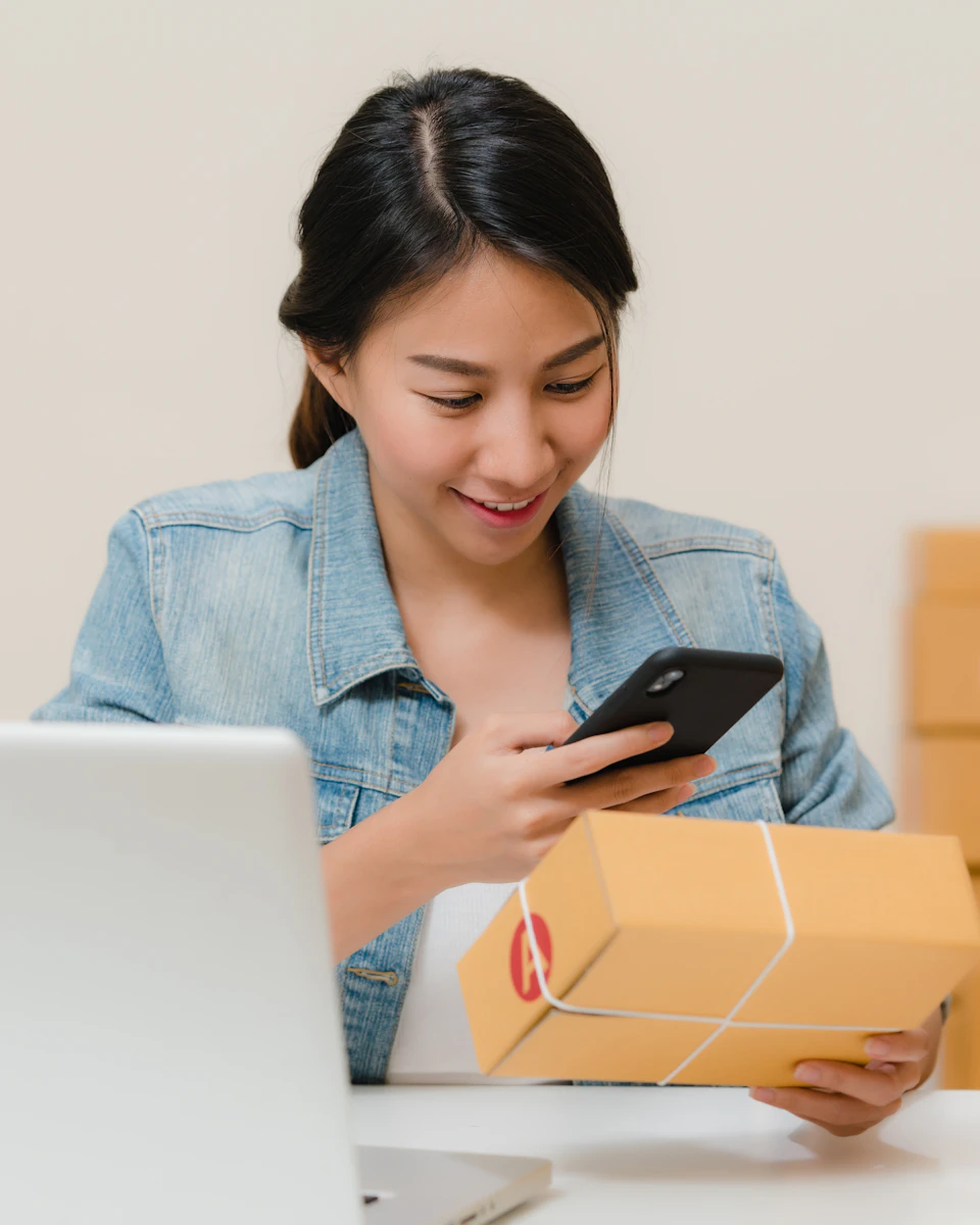 Amazon seller checking an order on her phone next to packed boxes and a laptop